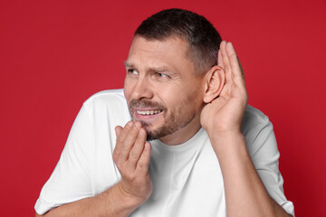 Man showing hand to ear gesture on red background