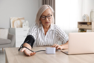 Woman measuring blood pressure at wooden table indoors