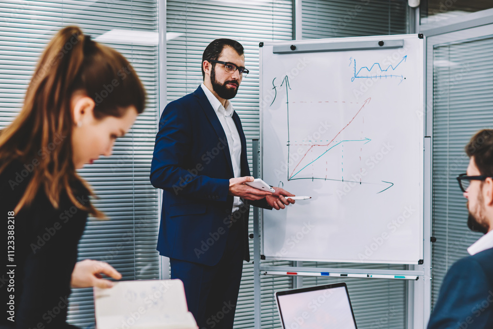 Poster experienced executive manager in spectacles standing next to flip chart and explaining for colleague