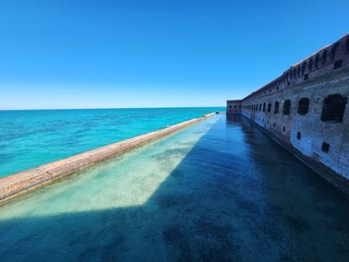 Fototapeta premium The waterfront view of Fort Jefferson with its brick structure stretching into the calm turquoise sea.
