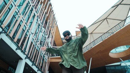 Low angle view of hipster pose in hip hop style surrounded by mall view. Portrait of sporty asian hip hop choreographer dancing break dance while looking at camera. Outdoor sport 2024. Hiphop.