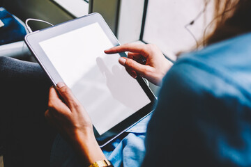 Obraz premium Rear view of young woman touching with finger on blank screen area of digital touch pad to choosing music application for installing on device via public wireless transport internet sitting in tram