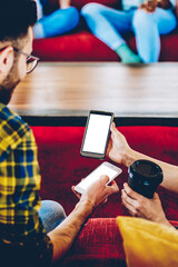 Cropped back view of male and female hipster bloggers discussing downloaded app on smartphone with...