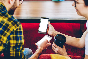 Cropped back view of male and female hipster bloggers discussing downloaded app on smartphone with...