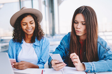 Positive female bloggers sharing media files via bluetooth connection on smartphone devices while...