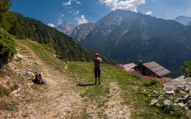 Fototapeta premium Hiker photographing alpine peaks near rustic cabin mountain landscape