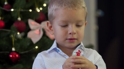 Happy child holding snow globe with figurine of Santa Claus. Smiling face of little boy near Christmas tree. Merry Christmas and Happy New year winter holidays.