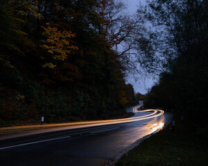 Langzeitbelichtung einer kurvigen Straße am Abend, die Lichtstreifen eines fahrenden Autos ziehen...