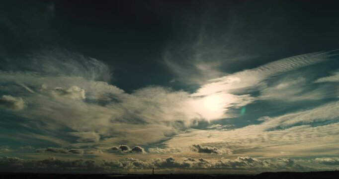 Wide Angle Time Lapse of Dark Low Horizon Under Expansive Blue Sky with Two Cloud Layers at Different Heights While Sunlight Breaks Dramatically Through High Veils Illuminating the Scene Below