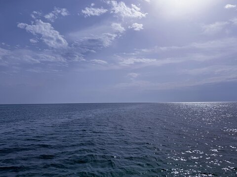 Ocean expanse blue shimmering water and cloudy sky. 