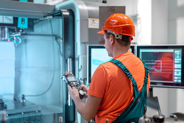 Male engineer operating cnc machine at factory. Technician in uniform and safety helmet  working at industrial workshop.