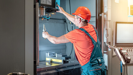 Male engineer operating cnc machine at factory. Technician in uniform and safety helmet  working at...