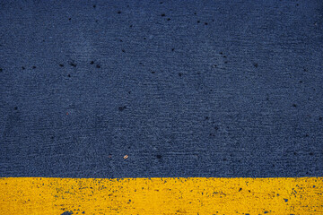 Closeup of a concrete surface featuring a striking yellow stripe on a dark gray asphalt background, ideal for urban, modern, and minimalistic photography themes.  Copy space