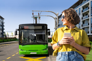 Woman with smartphone on the background of charging electric bus