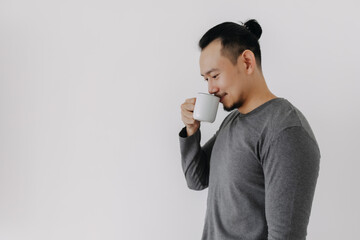Happy smile face Asian man in grey fleece base layer drinking hot drink on white.