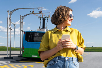 Woman with smartphone on the background of charging electric bus