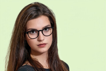 Obraz premium Portrait of long hair brunette girl with glasses posing on the light green. 