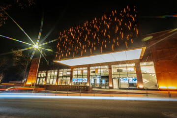 Valmiera Drama Theatre building illuminated with warm golden lights on its facade, contrasting the...