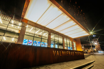 Valmiera Drama Theatre building illuminated with warm golden lights on its facade, contrasting the...
