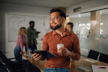 Smiling businessman holding digital tablet and takeaway coffee in modern office