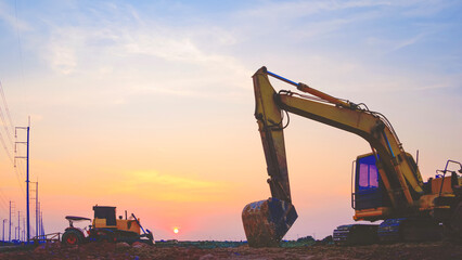 Silhouette of excavator and bulldozer tractor parked after work in land filling area for industrial factory construction site against sunset sky background © Prapat