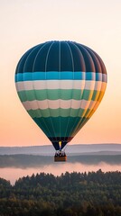 Obraz premium A vibrant hot air balloon floats above a misty landscape during sunset, showcasing colorful patterns against the soft sky.