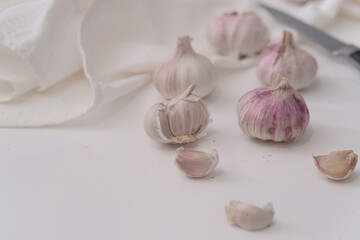 Heads of garlic are cut on a white kitchen table on a white marble board