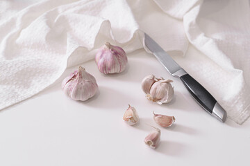 Heads of garlic are cut on a white kitchen table on a white marble board