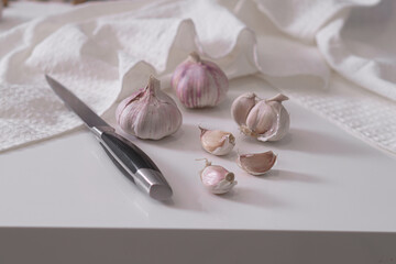 Heads of garlic are cut on a white kitchen table on a white marble board