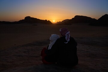 Tourist couple watching sunset in Wadi Rum desert, Jordan