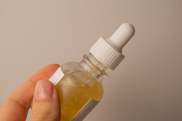 The face care serum in a glass jar with a white dispenser is in a woman's hand.