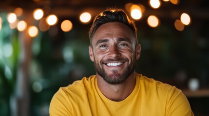 Obraz premium A confident bearded man wearing a marine yellow shirt grins warmly in a chic cafe, illuminated by soft glowing lights, capturing the essence of leisure and style.