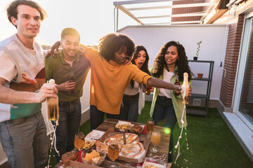 Friends making toast and spilling beer at rooftop party during sunset