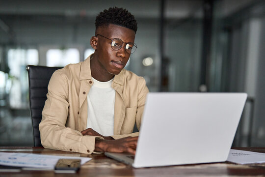 Busy Black business man employee or student using laptop. Serious professional African young company worker, male software developer typing on computer technology working elearning at office desk.