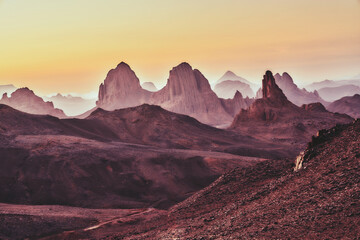 Naklejka premium Majestic Desert Landscape at Sunrise with Dramatic Mountain Peaks and Layers of Mist in the Horizon
