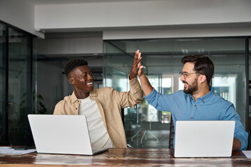 Two diverse happy professional business men employees team join hands giving high five celebrating...