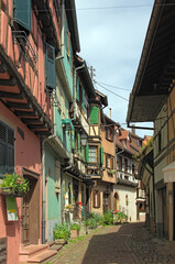 Obraz premium Charming cityscape view of narrow medieval cobblestone street between colorful stone houses in Eguisheim. Traditional architecture in Alsace in northeastern France. Travel and tourism concept