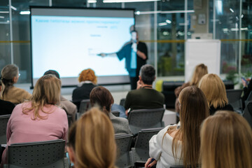 Fototapeta premium Diverse audience attentively listening to a business presentation in a modern conference room setting. Group is focused and engaged with the speaker.