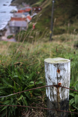 Fence pole with barbed wire on a field with small fishing village of Crovie in the background - Aberdeenshire - Scotland - UK © Collpicto