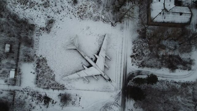 Aerial view of a Tupolev Tu-95 strategic bomber covered in snow, surrounded by trees and infrastructure in a winter setting.