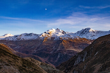 Snow covered mountain peaks and magic evening light over the Swiss Alps in autumn in the canton of...