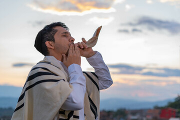 Young Jewish man blows the shofar at sunset to celebrate Rosh Hashanah or Jewish New Year