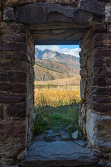 Naklejka premium ancient opening of an ancient stone building against the background of mountains and blue sky with clouds. Tourism and travel.