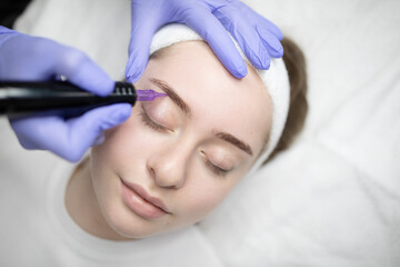 A skilled technician applies permanent makeup on a Caucasian client’s eyebrows, showcasing a...
