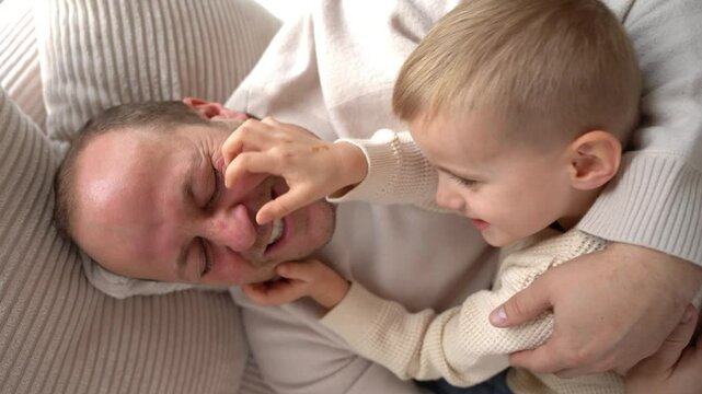 4-year-old son tickles his dad lying on the couch. High quality 4k footage