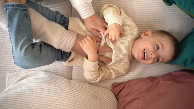 a dad tickles his 4-year-old son lying on the couch. High quality 4k footage