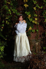 Fototapeta premium Young beautiful woman in vintage white dress standing in the evening garden