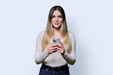 Young beautiful woman holding mobile phone, looking at camera on white studio background