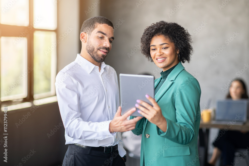Poster two professionals engage in discussion while sharing a tablet in a contemporary office environment. 