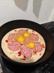 A pizza with eggs and salami inside a frying pan. Fried pizza.